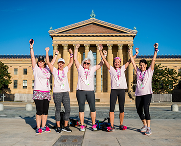 Five women pose with arms raised in victory
