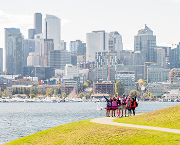 Walkers pose along waterfront with city skyline in the background